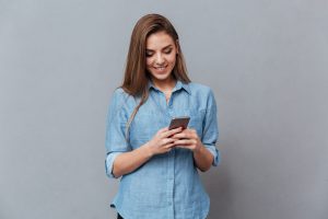 Smiling Woman in shirt using phone in studio. Isolated gray background